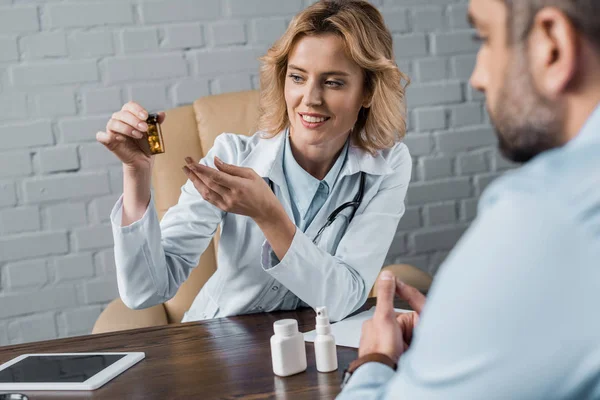 Улыбающаяся женщина-врач показывает банку с таблетками пациенту в офисе — стоковое фото
