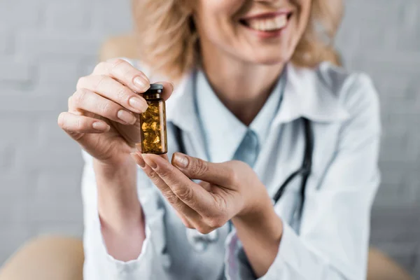 Cropped shot of smiling female doctor showing jar of pills to patient at office — Stock Photo