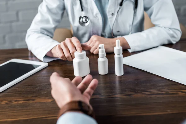 Inyección recortada de médico femenino que muestra varios medicamentos al paciente en el consultorio - foto de stock