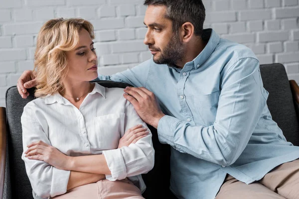 Homem falando com esposa enquanto sentado no sofá após briga — Fotografia de Stock