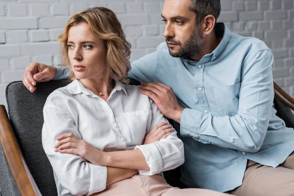 Hombre hablando con la esposa deprimida mientras está sentado en el sofá después de la discusión - foto de stock