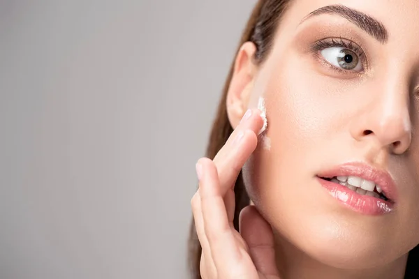 Beautiful woman applying face cream on perfect skin, isolated on grey — Stock Photo