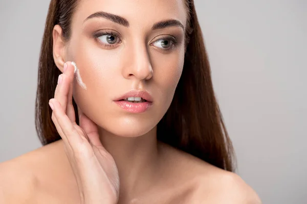 Ragazza che applica la crema viso sulla pelle pulita, isolata sul grigio — Foto stock