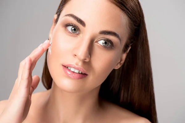 Beautiful woman applying anti-wrinkle cream on face, isolated on grey — Stock Photo