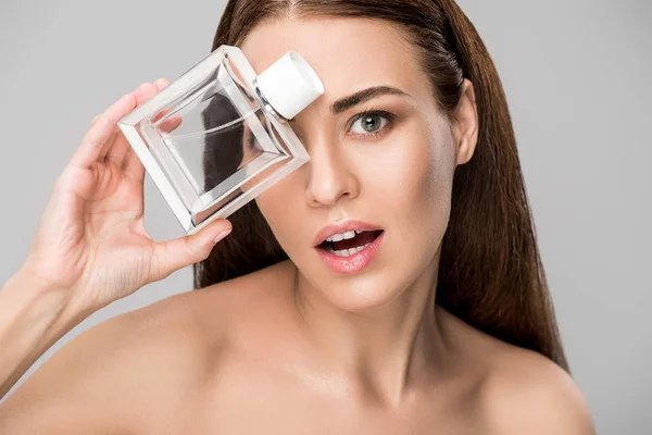 Beautiful surprised woman posing with perfume bottle isolated on grey — Stock Photo