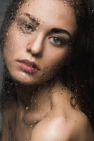 Attrayant fille derrière verre humide regardant caméra — Photo de stock