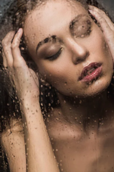 Beautiful tender woman with closed eyes behind wet glass — Stock Photo