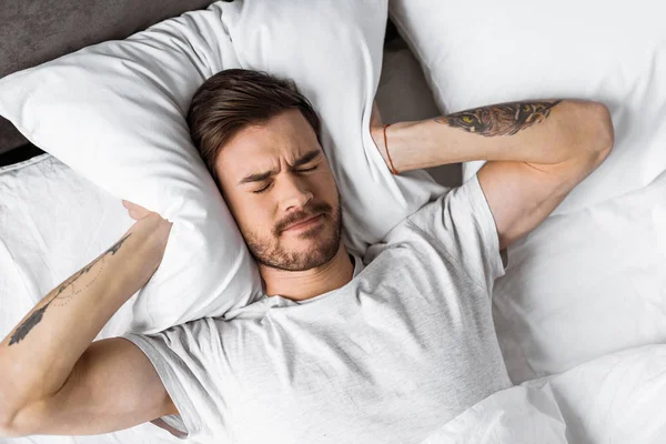 Vista superior do jovem que fecha as orelhas com travesseiro na cama pela manhã — Fotografia de Stock