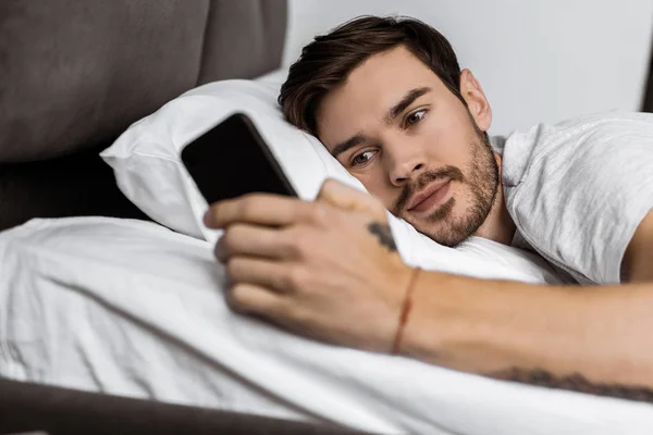 Schöner bärtiger junger Mann liegt im Bett und benutzt Smartphone — Stockfoto