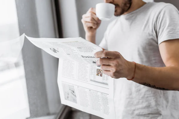 Tiro cortado de jovem bebendo café e lendo jornal pela manhã — Fotografia de Stock