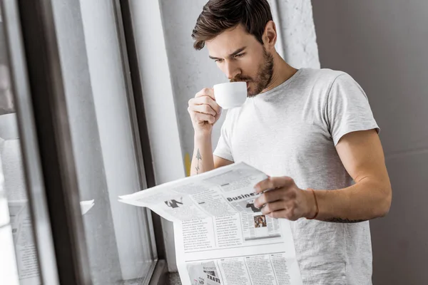 Joven guapo bebiendo café y leyendo el periódico en la mañana - foto de stock