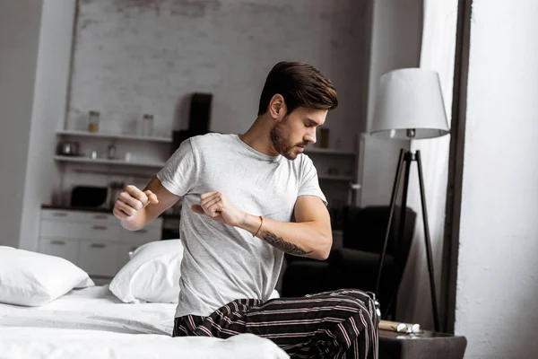 Young man in pajamas exercising and stretching while sitting in bed in the morning — Stock Photo