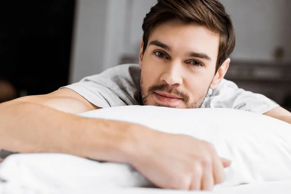 Schöner junger Mann, der auf dem Bett liegt und in die Kamera schaut — Stockfoto