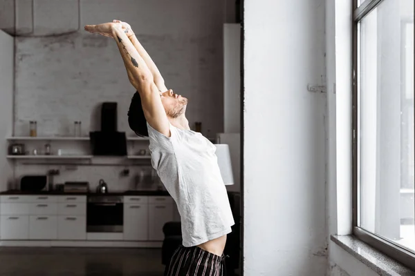 Side view of young man in pajamas stretching hands in the morning at home — Stock Photo