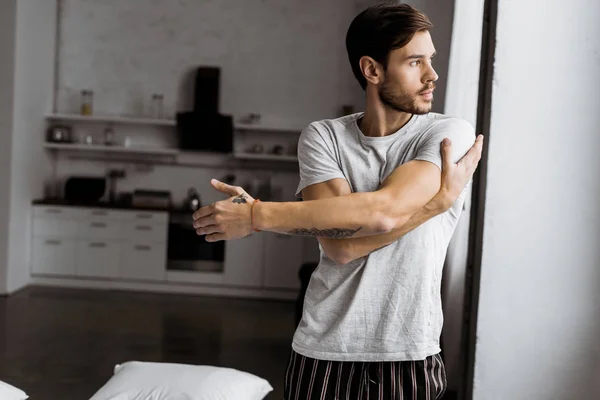 Schöner junger Mann im Pyjama, der morgens zu Hause trainiert und wegschaut — Stockfoto