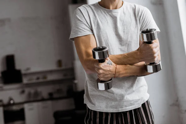 Tiro cortado de jovem em pijama segurando halteres em casa — Fotografia de Stock