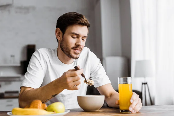 Schöner junger Mann mit Müsli mit Orangensaft zu Hause — Stockfoto