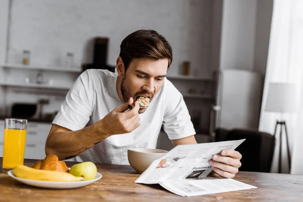 Junger Mann isst Müsli zum Frühstück und liest Zeitung zu Hause — Stockfoto