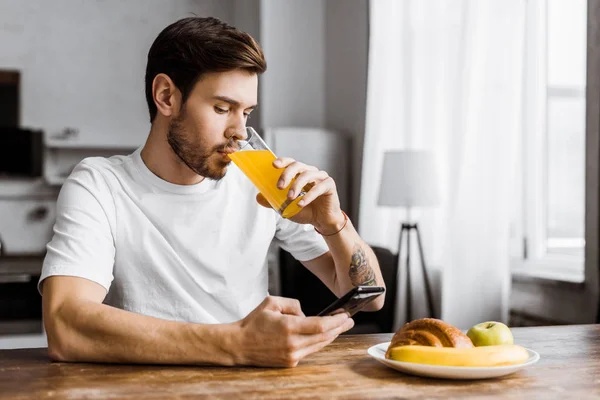 Attraktiver junger Mann nutzt Smartphone beim Frühstück zu Hause — Stockfoto