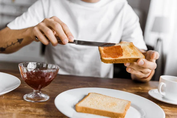 Cropped shot of man applying jam onto toast at home — Stock Photo
