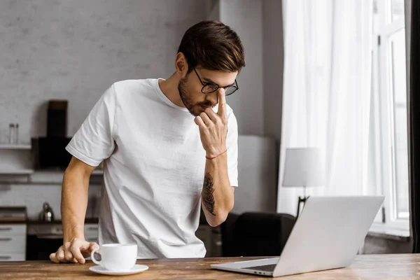 Attrayant jeune pigiste avec café et ordinateur portable sur la cuisine à la maison — Photo de stock