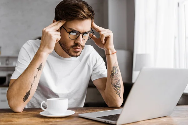 Concentré jeune pigiste avec café travaillant avec ordinateur portable à la maison — Photo de stock