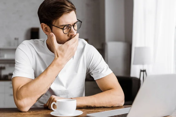 Bostezando joven freelancer con café trabajando con portátil en casa - foto de stock