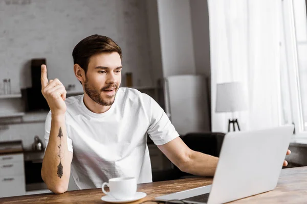 Excited young man with coffee using laptop and looking up at home — Stock Photo