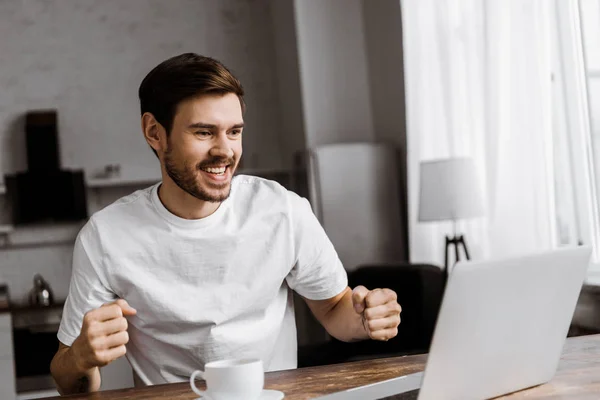 Jovem emocional com café usando laptop em casa — Fotografia de Stock