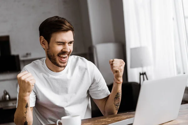 Celebrating young man with coffee using laptop at home — Stock Photo