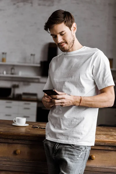 Handsome young man using smartphone on kitchen at home — Stock Photo