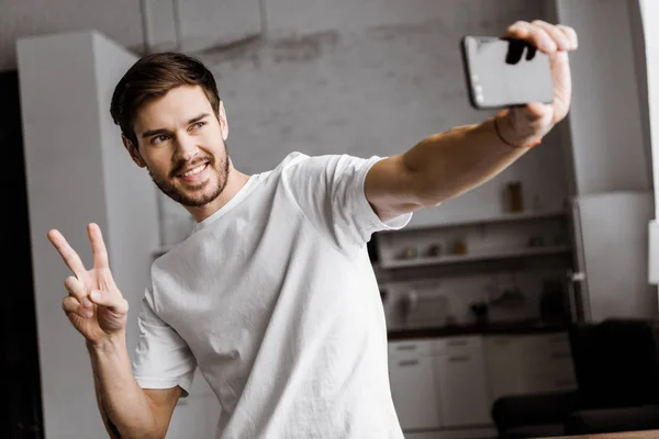 Schöner junger Mann macht Selfie und macht Friedensgeste zu Hause — Stockfoto