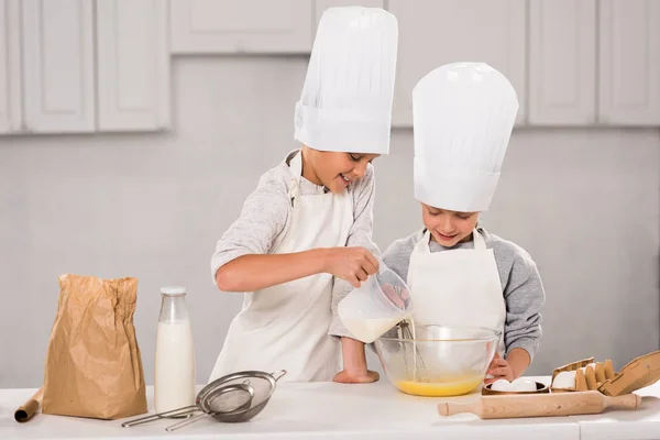 Ragazzo versando il latte in ciotola mentre sorella in piedi vicino a tavola in cucina — Foto stock