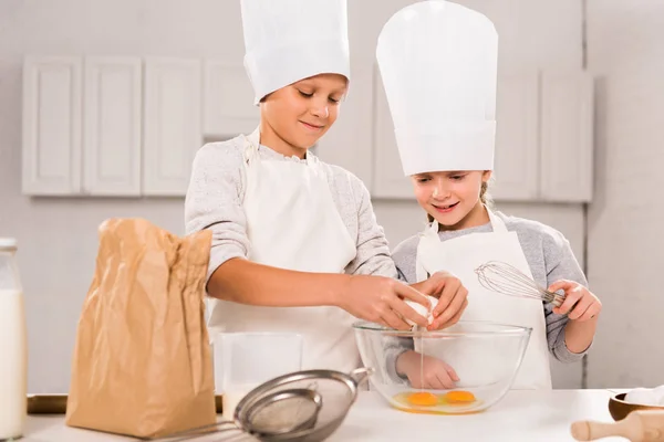 Усміхнена сестра і брат розбивають яйця в миску під час приготування їжі за столом на кухні — стокове фото