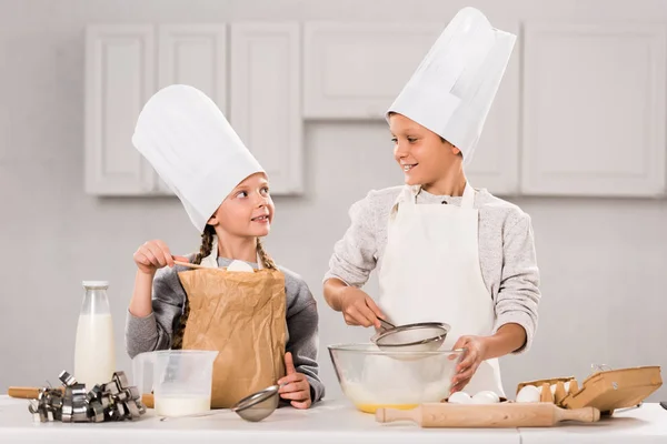 Bambini piccoli in grembiuli e cappelli da chef che si preparano a tavola in cucina — Foto stock