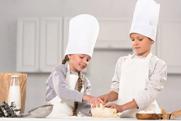 Улыбающиеся брат и сестра готовят тесто для печенья за столом на кухне — стоковое фото