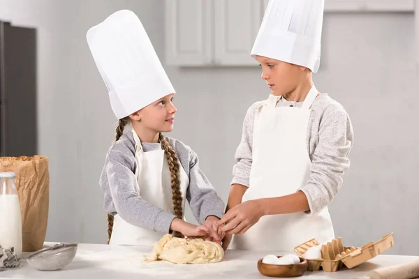 Irmão e irmã preparando massa para biscoitos à mesa na cozinha — Fotografia de Stock