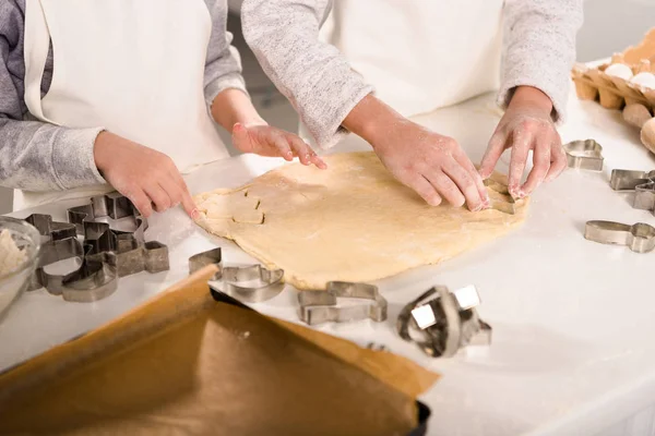 Cropped image of kids in aprons cutting out dough for cookies at table in kitchen — Stock Photo