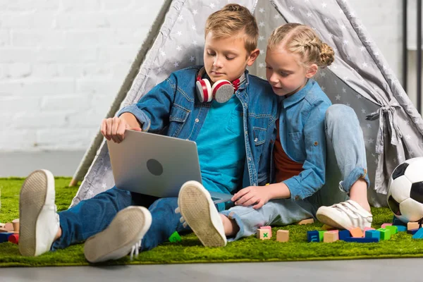 Adorable little brother and sister using laptop near tent at home — Stock Photo