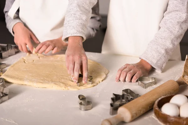 Visão parcial de crianças em aventais cortando a massa de farinha de biscoitos à mesa na cozinha — Fotografia de Stock