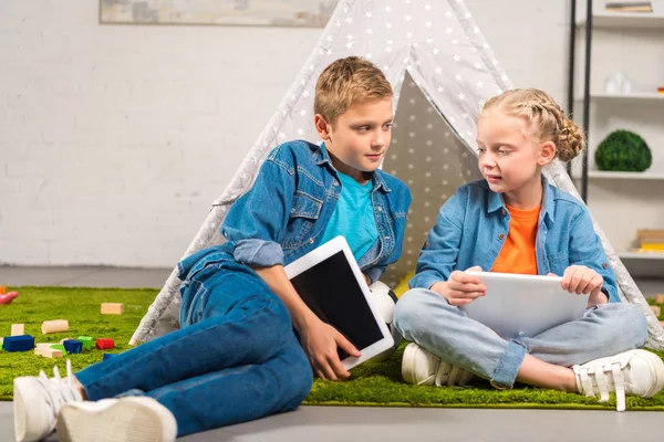 Irmã e irmão com tablets digitais perto wigwam em casa — Fotografia de Stock