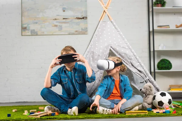 Hermano y hermana usando auriculares de realidad virtual cerca de wigwam en casa - foto de stock