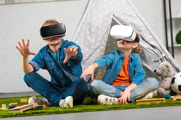 Bambini che usano cuffie di realtà virtuale e gesticolano con le mani vicino a wigwam a casa — Foto stock