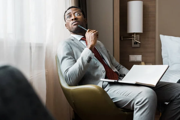 Homme d'affaires afro-américain réfléchi avec journal intime assis dans la chambre d'hôtel — Photo de stock