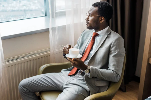 Empresario afroamericano sosteniendo taza de café y mirando a la ventana - foto de stock