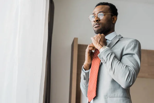Belo empresário afro-americano ajustando gravata vermelha no quarto de hotel — Fotografia de Stock