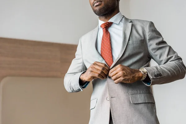 Vista cortada de empresário afro-americano abotoando jaqueta cinza — Fotografia de Stock
