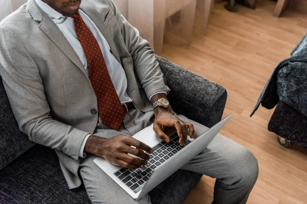 Vue recadrée de l'homme d'affaires afro-américain tapant sur ordinateur portable dans la chambre d'hôtel — Photo de stock