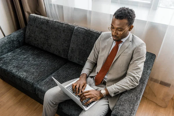 Elegante hombre de negocios afroamericano utilizando el ordenador portátil en la habitación de hotel - foto de stock