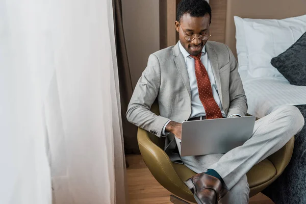 Bell'uomo d'affari afro-americano sorridente che lavora su laptop in camera d'albergo — Foto stock